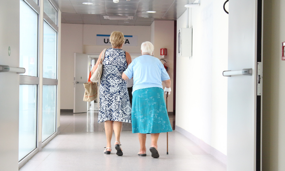 elderly woman walking down hospital hallway.